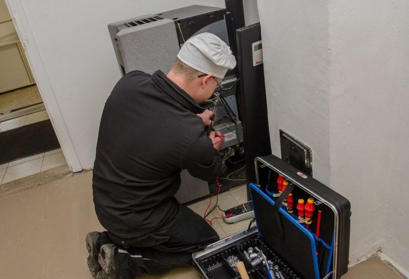 Rauchfangkehrer in dunkler Uniform bei der Inspektion eines Pelletofens